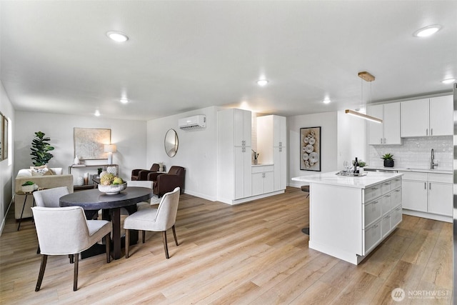 4126 19th Ave SW, Seattle, WA 98106 - kitchen with a sink, light wood-type flooring, a wall mounted AC, a kitchen island, and white cabinetry