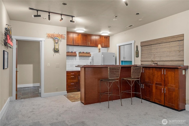 10507 48th St E, Edgewood, WA 98372 - kitchen with freestanding refrigerator, light carpet, brown cabinetry, a kitchen bar, and rail lighting