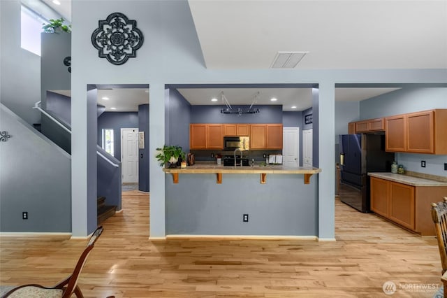 782 Fenway Ln SW, Tumwater, WA 98512 - kitchen with black appliances, a kitchen bar, light wood-style flooring, tile countertops, and a peninsula