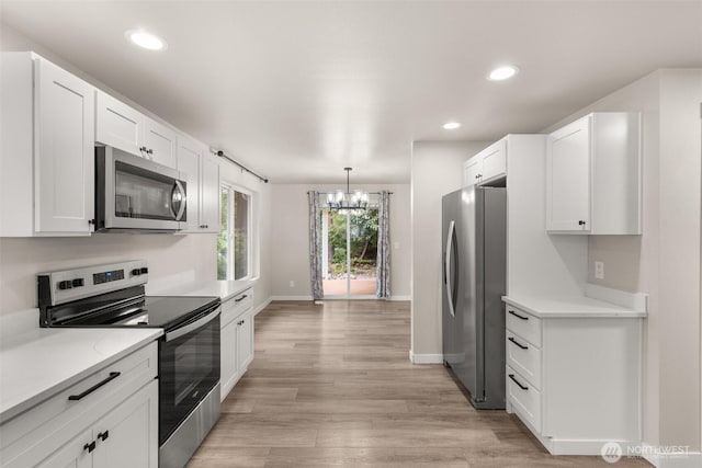 18822 Rampart Dr SE, Yelm, WA 98597 - kitchen with stainless steel appliances, a chandelier, white cabinetry, light wood finished floors, and recessed lighting