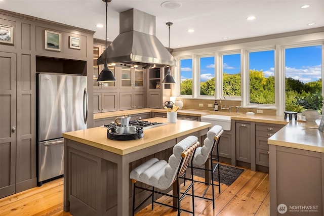 1237 Hawley Way NE, Bainbridge Island, WA 98110 - kitchen with appliances with stainless steel finishes, island exhaust hood, light wood-style flooring, a kitchen island, and a kitchen bar