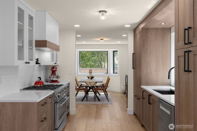 7201 Seward Park Ave S, Seattle, WA 98118 - kitchen with appliances with stainless steel finishes, a sink, light wood finished floors, glass insert cabinets, and light countertops