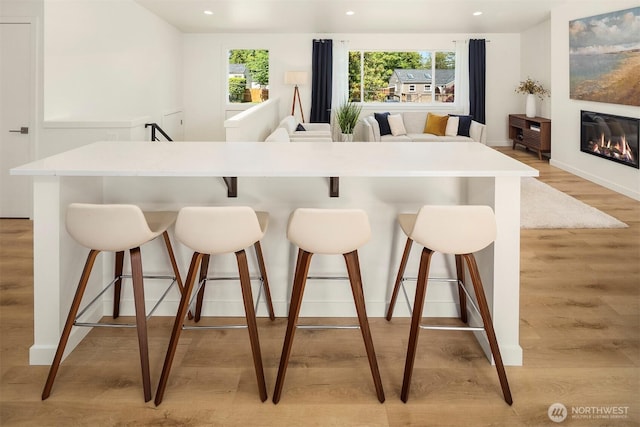 303 NE 133rd St, Seattle, WA 98125 - kitchen with light wood-style floors, recessed lighting, a breakfast bar, a glass covered fireplace, and light countertops