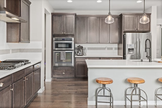 303 Vaughan Blvd NE, North Bend, WA 98045 - kitchen featuring wall chimney range hood, stainless steel appliances, a breakfast bar area, dark brown cabinetry, and recessed lighting