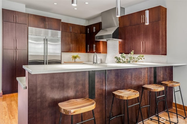2334 N 57th St, Seattle, WA 98103 - kitchen featuring built in refrigerator, wall chimney range hood, light wood-style floors, light countertops, and backsplash