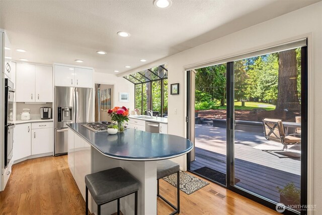 2911 216th Ave NE, Sammamish, WA 98074 - kitchen with appliances with stainless steel finishes, light wood-type flooring, white cabinets, a breakfast bar area, and recessed lighting