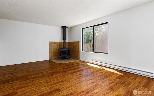 111 NW Columbia Dr Unit B7, Oak Harbor, WA 98277 - unfurnished living room featuring a wood stove, wood finished floors, a baseboard heating unit, a textured ceiling, and baseboards