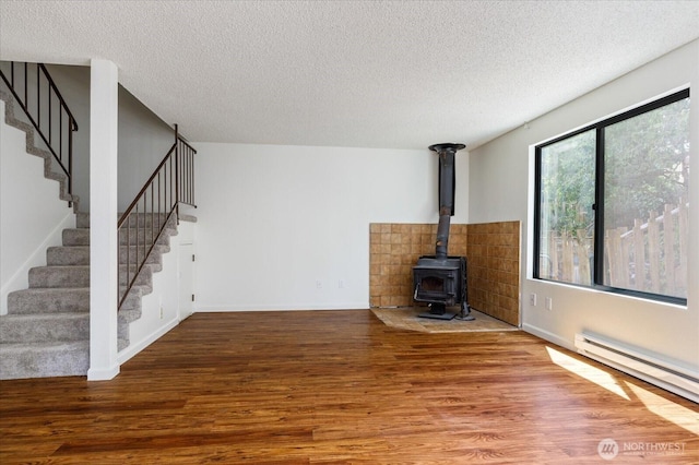 111 NW Columbia Dr Unit B7, Oak Harbor, WA 98277 - unfurnished living room featuring a baseboard heating unit, wood finished floors, stairway, a wood stove, and a textured ceiling