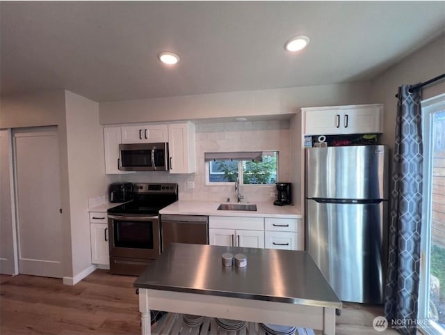 1042 S Donovan St Unit 5, Seattle, WA 98108 - kitchen with appliances with stainless steel finishes, a sink, backsplash, white cabinetry, and light wood-style flooring