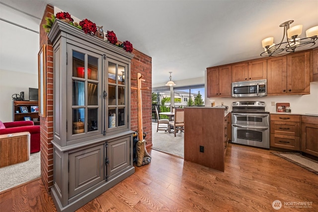 2360 43rd Ave E Unit 302, Seattle, WA 98112 - kitchen featuring stainless steel appliances, light wood finished floors, a chandelier, hanging light fixtures, and brown cabinetry