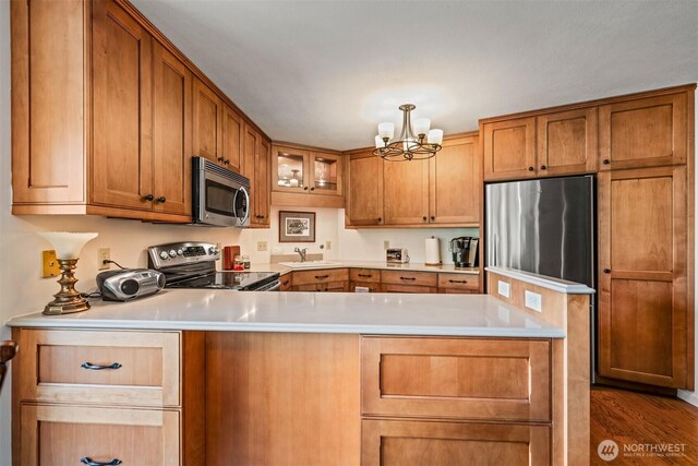 2360 43rd Ave E Unit 302, Seattle, WA 98112 - kitchen with stainless steel appliances, a chandelier, brown cabinets, light countertops, and glass insert cabinets