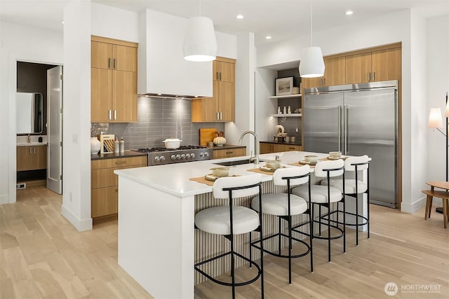 5822 56th Ave NE, Seattle, WA 98105 - kitchen with stainless steel built in fridge, light wood-style floors, a center island with sink, backsplash, and a kitchen breakfast bar