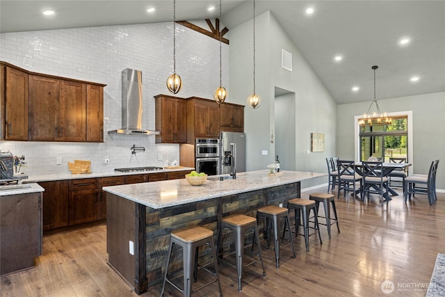1550 Old Cedars Rd, Cle Elum, WA 98922 - kitchen with wall chimney exhaust hood, high vaulted ceiling, appliances with stainless steel finishes, a center island with sink, and wood finished floors