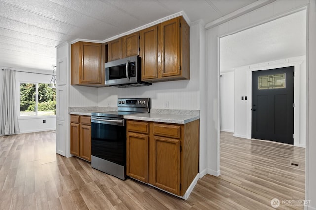 17107 Snowbell Ct SE, Yelm, WA 98597 - kitchen featuring appliances with stainless steel finishes, brown cabinets, light countertops, light wood-type flooring, and ornamental molding