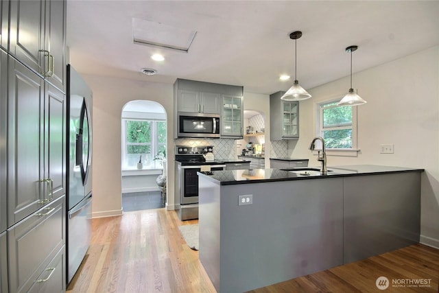 719 N 92nd St, Seattle, WA 98103 - kitchen featuring appliances with stainless steel finishes, a sink, a peninsula, gray cabinets, and glass insert cabinets