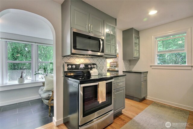 719 N 92nd St, Seattle, WA 98103 - kitchen featuring stainless steel appliances, gray cabinets, light wood-type flooring, glass insert cabinets, and dark countertops