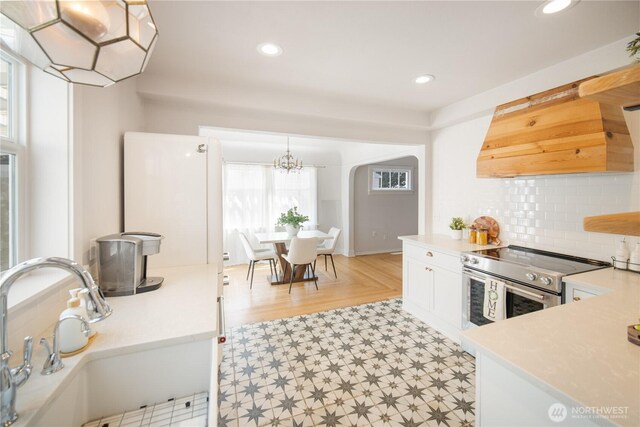707 Ryan Ave, Sumner, WA 98390 - kitchen with stainless steel range with electric cooktop, custom exhaust hood, light countertops, arched walkways, and backsplash