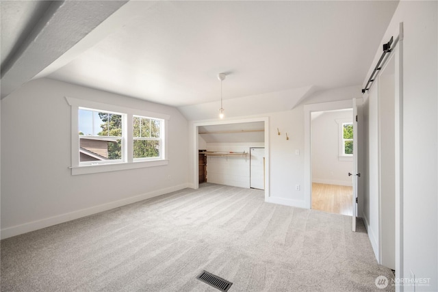 707 Ryan Ave, Sumner, WA 98390 - unfurnished bedroom featuring light carpet, vaulted ceiling, multiple windows, a barn door, and a closet