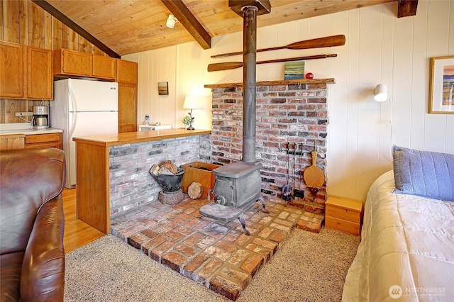 881 Lawson Rd, Camano Island, WA 98282 - kitchen with freestanding refrigerator, a wood stove, wooden ceiling, brown cabinetry, and wood walls