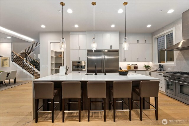 1201 222nd Ct SE, Sammamish, WA 98075 - kitchen with high quality appliances, a sink, wall chimney range hood, light wood-style floors, and a large island