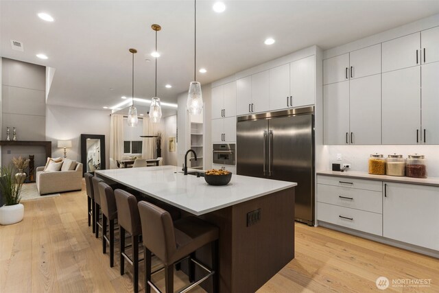 1201 222nd Ct SE, Sammamish, WA 98075 - kitchen with appliances with stainless steel finishes, light wood-type flooring, a breakfast bar, a center island with sink, and white cabinetry