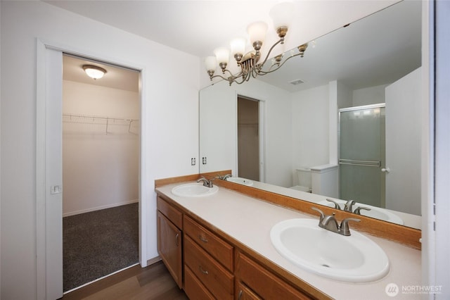 1105 200th Street Ct E, Spanaway, WA 98387 - bathroom featuring double vanity, a shower stall, a chandelier, wood finished floors, and a walk in closet