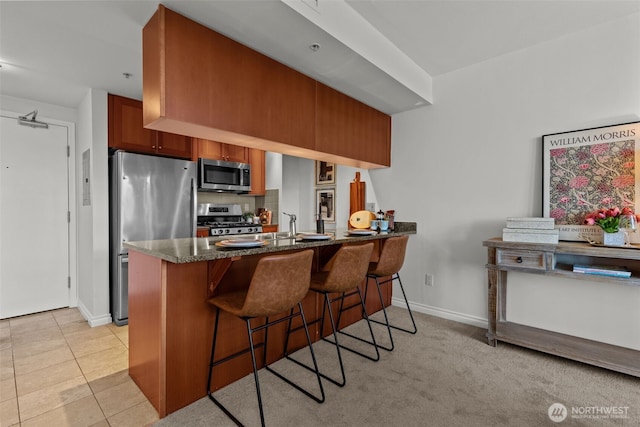 1420 Terry Ave Unit 1203, Seattle, WA 98101 - kitchen featuring stainless steel appliances, baseboards, dark stone countertops, a peninsula, and a breakfast bar area