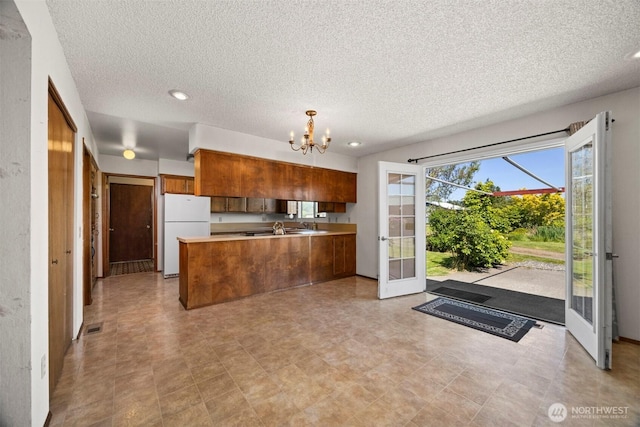 1119 Sunset Ave, Bellingham, WA 98226 - kitchen with freestanding refrigerator, a peninsula, brown cabinets, a chandelier, and a textured ceiling