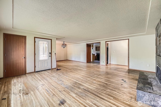 1001 Fairway Dr, Fircrest, WA 98466 - unfurnished living room featuring a textured ceiling, light wood finished floors, a chandelier, baseboards, and a large fireplace