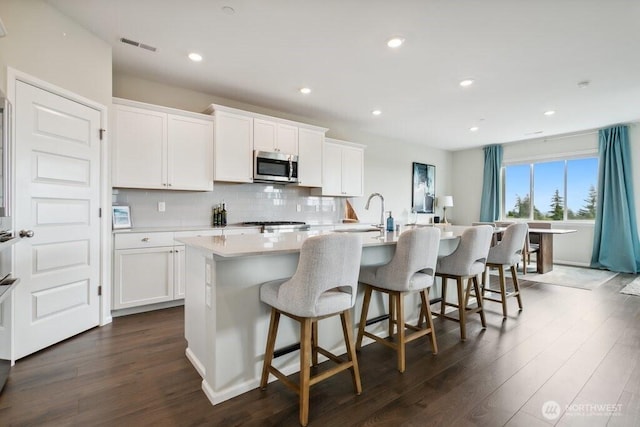 1134 Baker Heights Loop, Bremerton, WA 98312 - kitchen featuring stainless steel microwave, a center island with sink, dark wood-type flooring, decorative backsplash, and recessed lighting