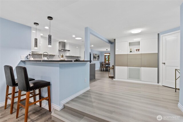 4530 240th St SW, Mountlake Terrace, WA 98043 - kitchen featuring wall chimney range hood, light wood-style flooring, white cabinets, a kitchen breakfast bar, and a peninsula