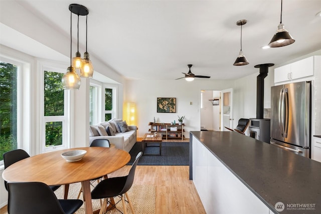 1188 Island Dr, Lummi Island, WA 98262 - kitchen with freestanding refrigerator, white cabinetry, light wood-style flooring, a wood stove, and hanging light fixtures