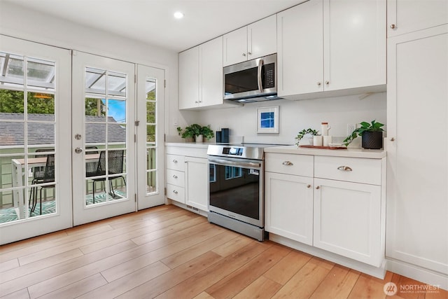 369 NW 49th St, Seattle, WA 98107 - kitchen featuring appliances with stainless steel finishes, light countertops, white cabinetry, light wood-style floors, and recessed lighting