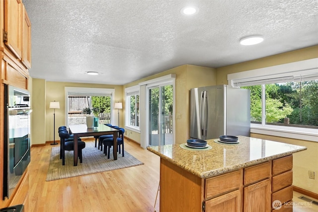 6149 115th Pl SE, Bellevue, WA 98006 - kitchen featuring stainless steel appliances, a textured ceiling, light wood-type flooring, a kitchen island, and light stone countertops
