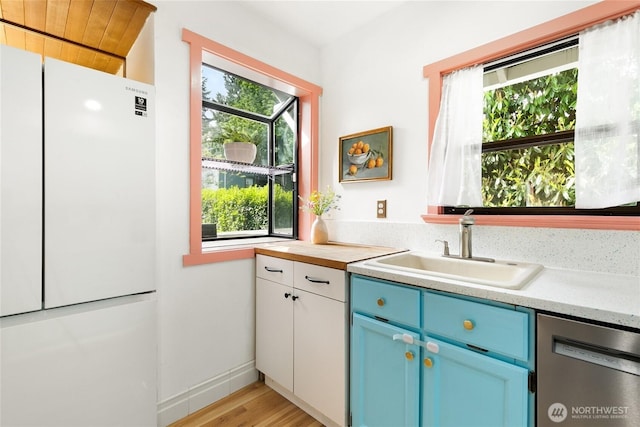 7141 47th Ave SW, Seattle, WA 98136 - kitchen with freestanding refrigerator, stainless steel dishwasher, a sink, blue cabinets, and light countertops
