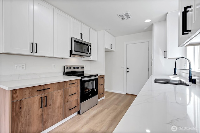 20610 6th Avenue Ct E, Spanaway, WA 98387 - kitchen with stainless steel appliances, a sink, light wood-style floors, light stone countertops, and white cabinets
