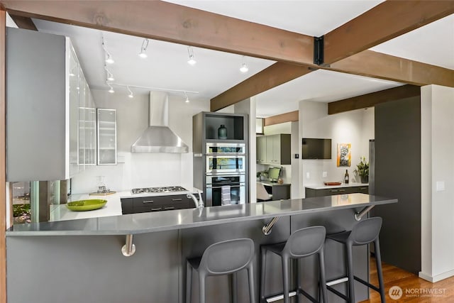 2019 Killarney Way, Bellevue, WA 98004 - kitchen featuring wall chimney exhaust hood, stainless steel appliances, wood finished floors, a peninsula, and a breakfast bar area