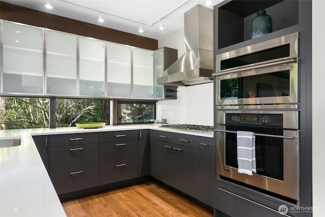 2019 Killarney Way, Bellevue, WA 98004 - kitchen featuring appliances with stainless steel finishes, wall chimney exhaust hood, modern cabinets, light countertops, and light wood-type flooring