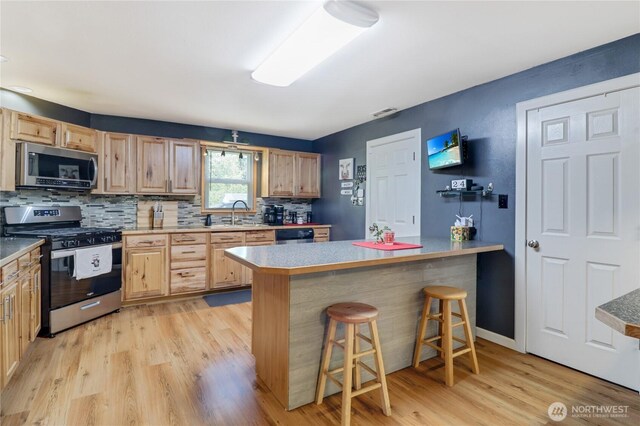 108 2nd St SE, Rainier, WA 98576 - kitchen featuring appliances with stainless steel finishes, light brown cabinetry, light wood-type flooring, a breakfast bar, and backsplash
