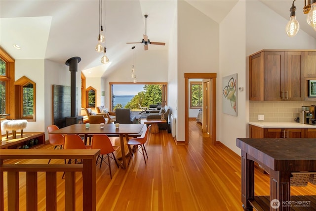 815 Carefree Way, Friday Harbor, WA 98250 - dining room featuring a wood stove, ceiling fan, light wood finished floors, high vaulted ceiling, and radiator