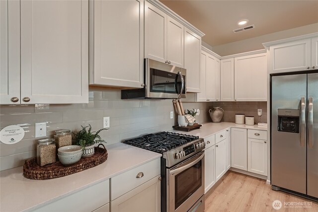 13461 192nd St E, Graham, WA 98338 - kitchen with stainless steel appliances, light countertops, white cabinets, backsplash, and light wood-style flooring