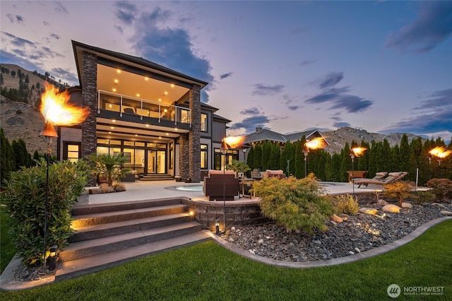 106 Shypoke Pl, Entiat, WA 98822 - back of property at dusk featuring a patio area, a balcony, stone siding, and a hot tub