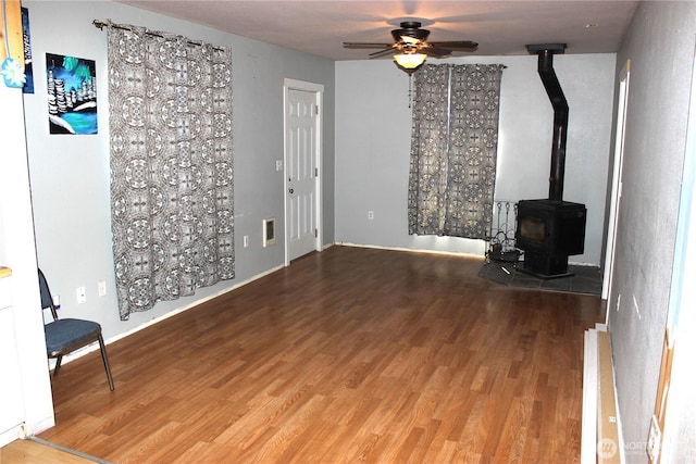 18343 Albany St SW, Rochester, WA 98579 - unfurnished living room featuring wood finished floors, a ceiling fan, a wood stove, radiator, and baseboards