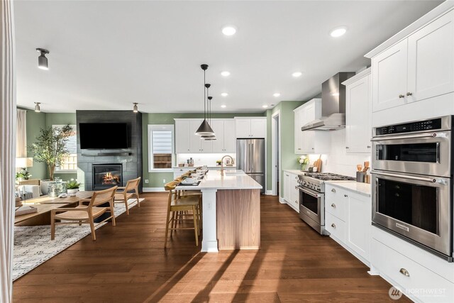 15306 204th Ave E Unit 23, Bonney Lake, WA 98391 - kitchen featuring stainless steel appliances, wall chimney exhaust hood, open floor plan, light countertops, and a fireplace