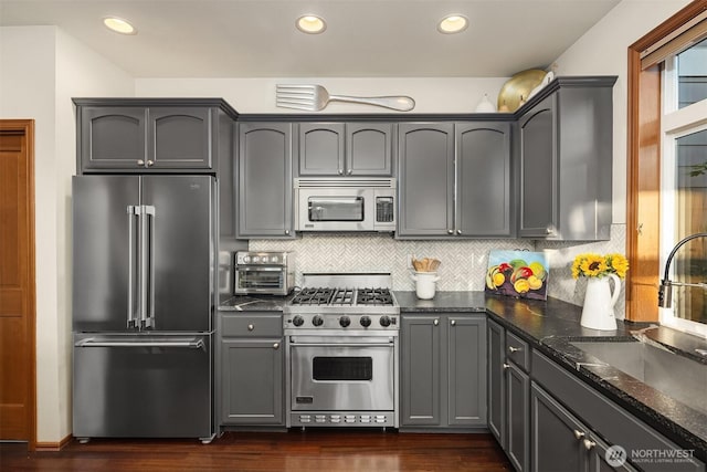 5613 21st Ave SW, Seattle, WA 98106 - kitchen featuring premium appliances, gray cabinets, dark wood-style floors, dark stone countertops, and decorative backsplash
