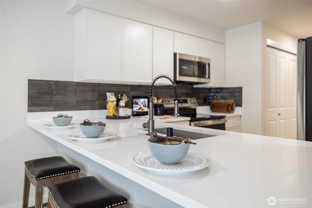 11215 NE 128th St Unit L-203, Kirkland, WA 98034 - kitchen featuring stainless steel appliances, tasteful backsplash, light countertops, white cabinetry, and a kitchen breakfast bar