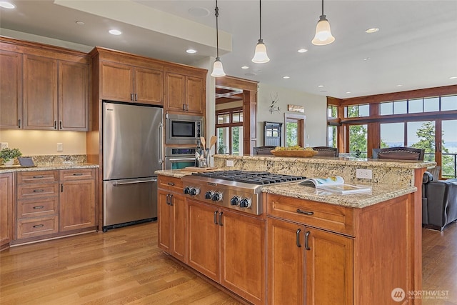 3430 Sevenich Dr, Everett, WA 98201 - kitchen with appliances with stainless steel finishes, light wood-style floors, brown cabinetry, pendant lighting, and light stone countertops