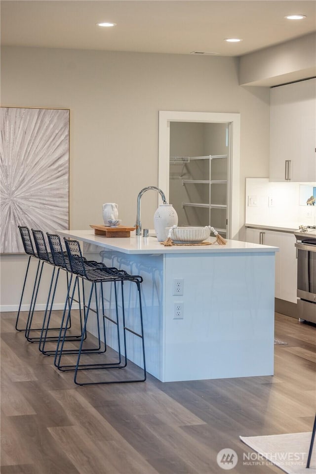 33488 Golden Lakes Ln SE, Black Diamond, WA 98010 - kitchen featuring white cabinetry, stainless steel stove, wood finished floors, a kitchen bar, and recessed lighting