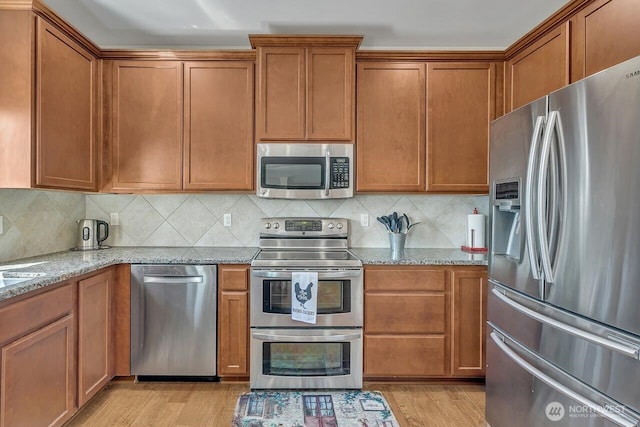 6715 Quincy Ave SE, Auburn, WA 98092 - kitchen featuring appliances with stainless steel finishes, brown cabinets, light stone countertops, light wood-type flooring, and decorative backsplash