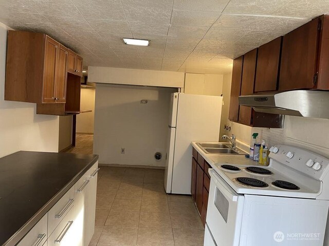 27 SW 102nd St, Seattle, WA 98146 - kitchen with white appliances, under cabinet range hood, a sink, light tile patterned floors, and brown cabinets